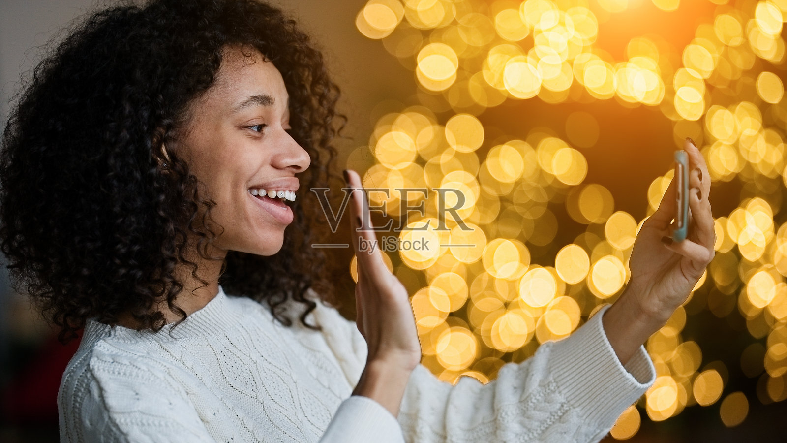 一名非裔美国妇女在圣诞树旁用智能手机视频聊天照片摄影图片