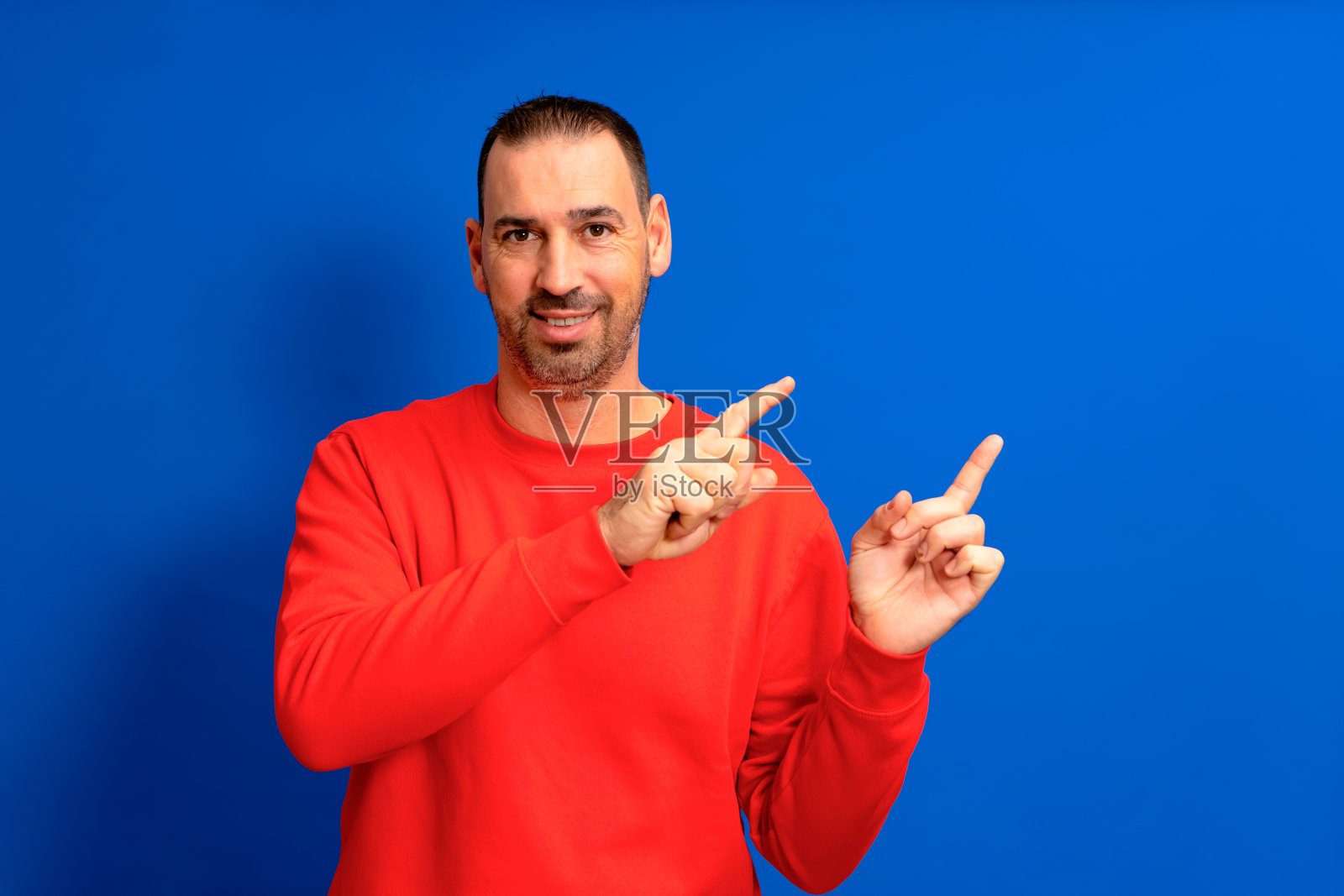 留着胡子的西班牙男子指着食指,在复制空间中模拟孤立在蓝色背景的工作室肖像。照片摄影图片