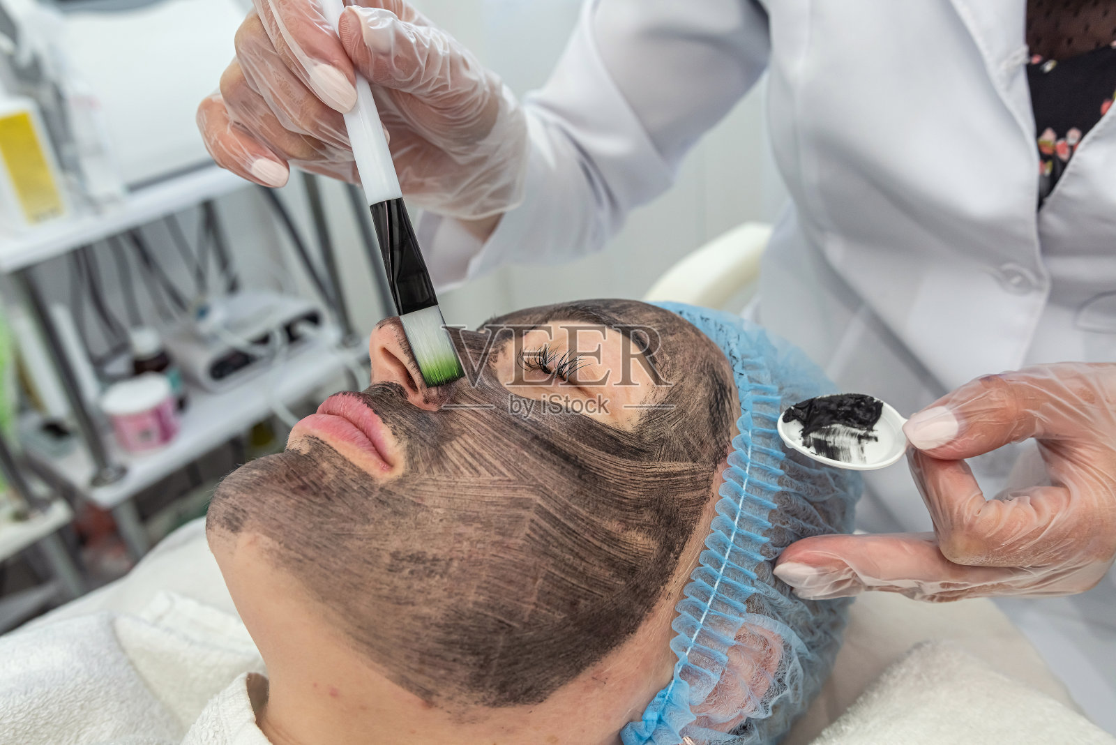 在水疗沙龙里,用刷子把粘土面膜涂在放松的女人脸上。照片摄影图片