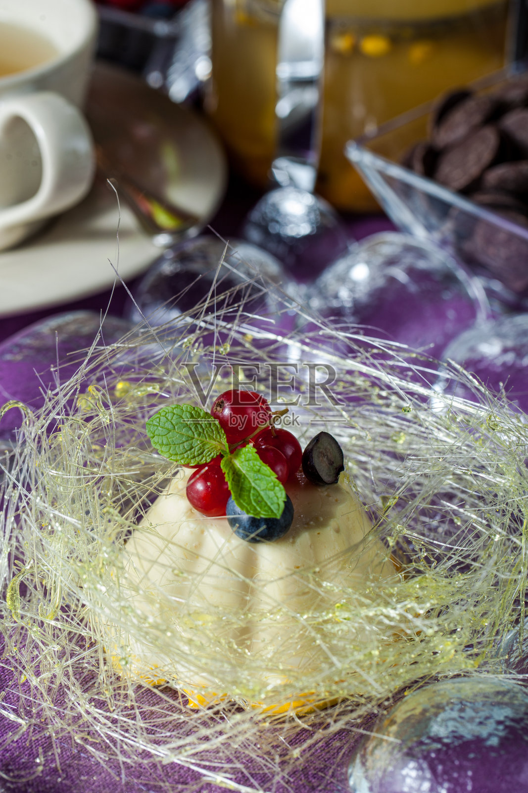 甜点焦糖布丁,糖线,红醋栗和蓝莓在紫色糖的背景。水平方向照片摄影图片