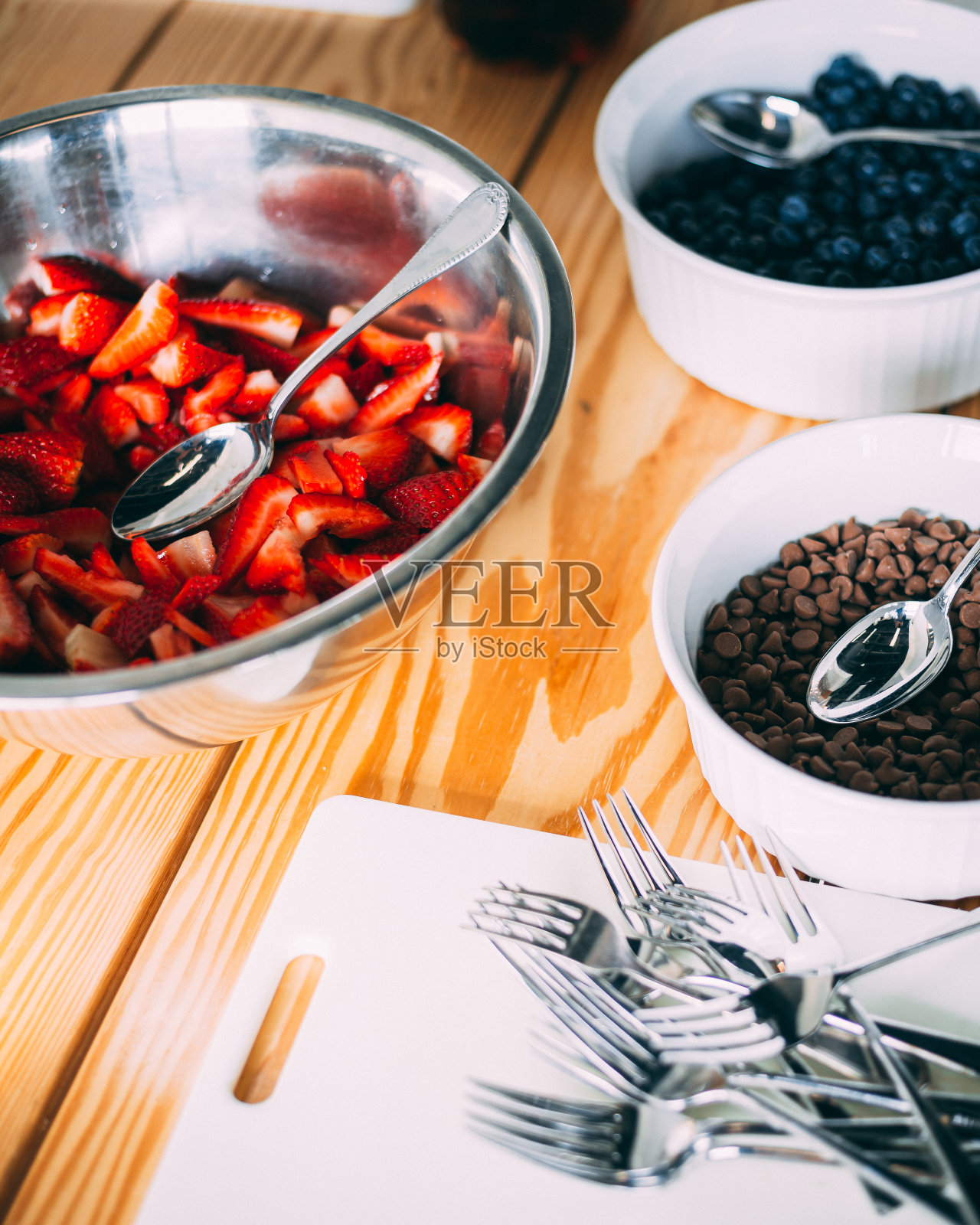 草莓、蓝莓和巧克力放在碗里,叉子放在木桌上的白板上。照片摄影图片