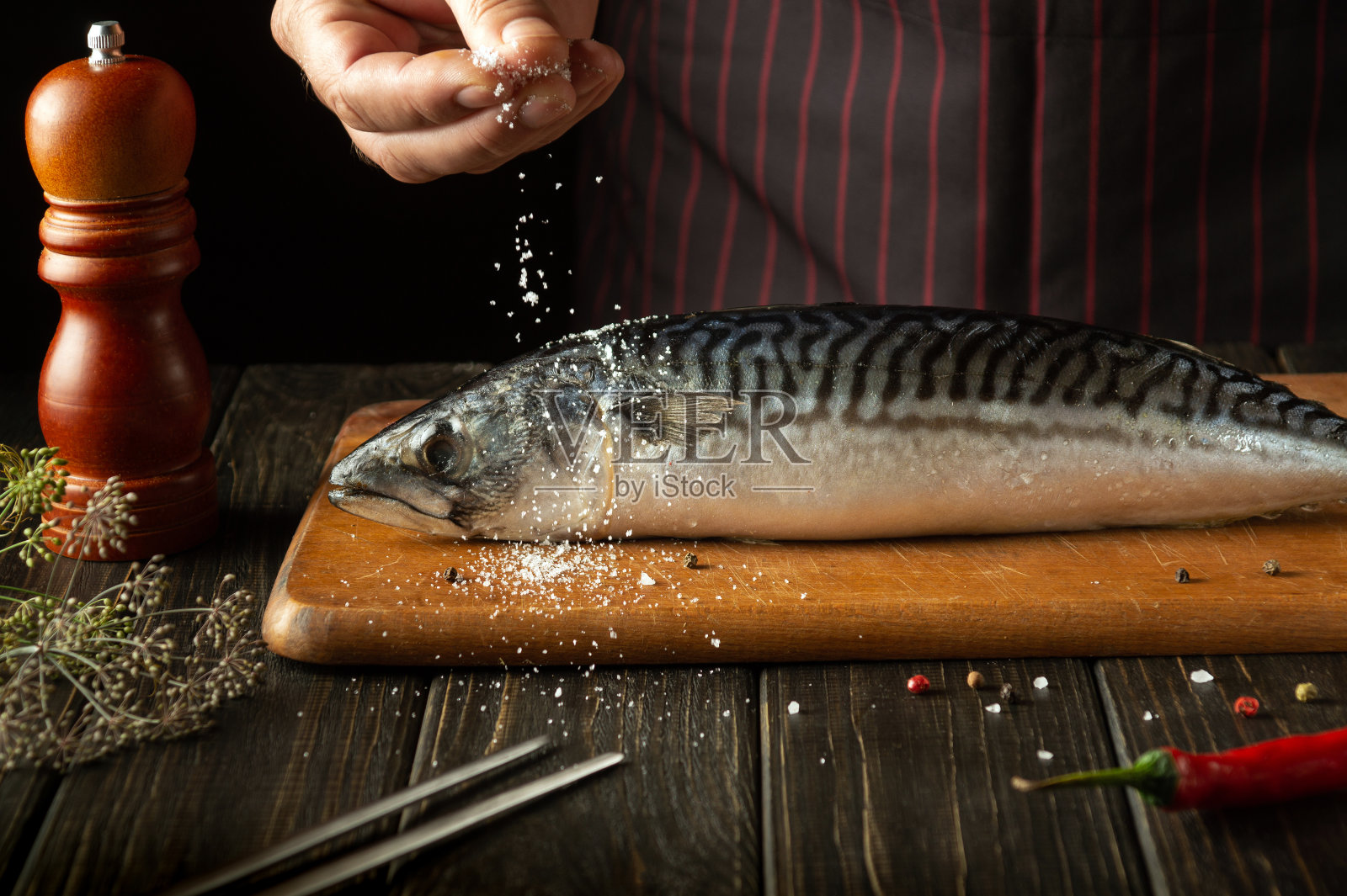 厨师正在厨房里给斯科姆鱼加盐。根据餐馆的特殊食谱烹调鱼照片摄影图片