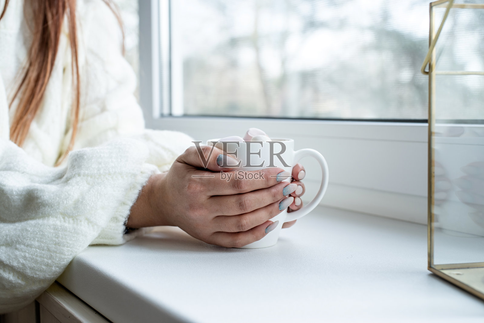 女人手在温暖的白色冬季毛衣坐在窗台在平安夜在家里拿着一杯棉花糖照片摄影图片