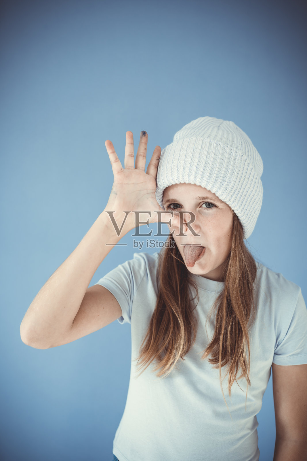 酷女孩与冬季羊毛无帽帽是站在前面的蓝色背景和做鬼脸,脸照片摄影图片