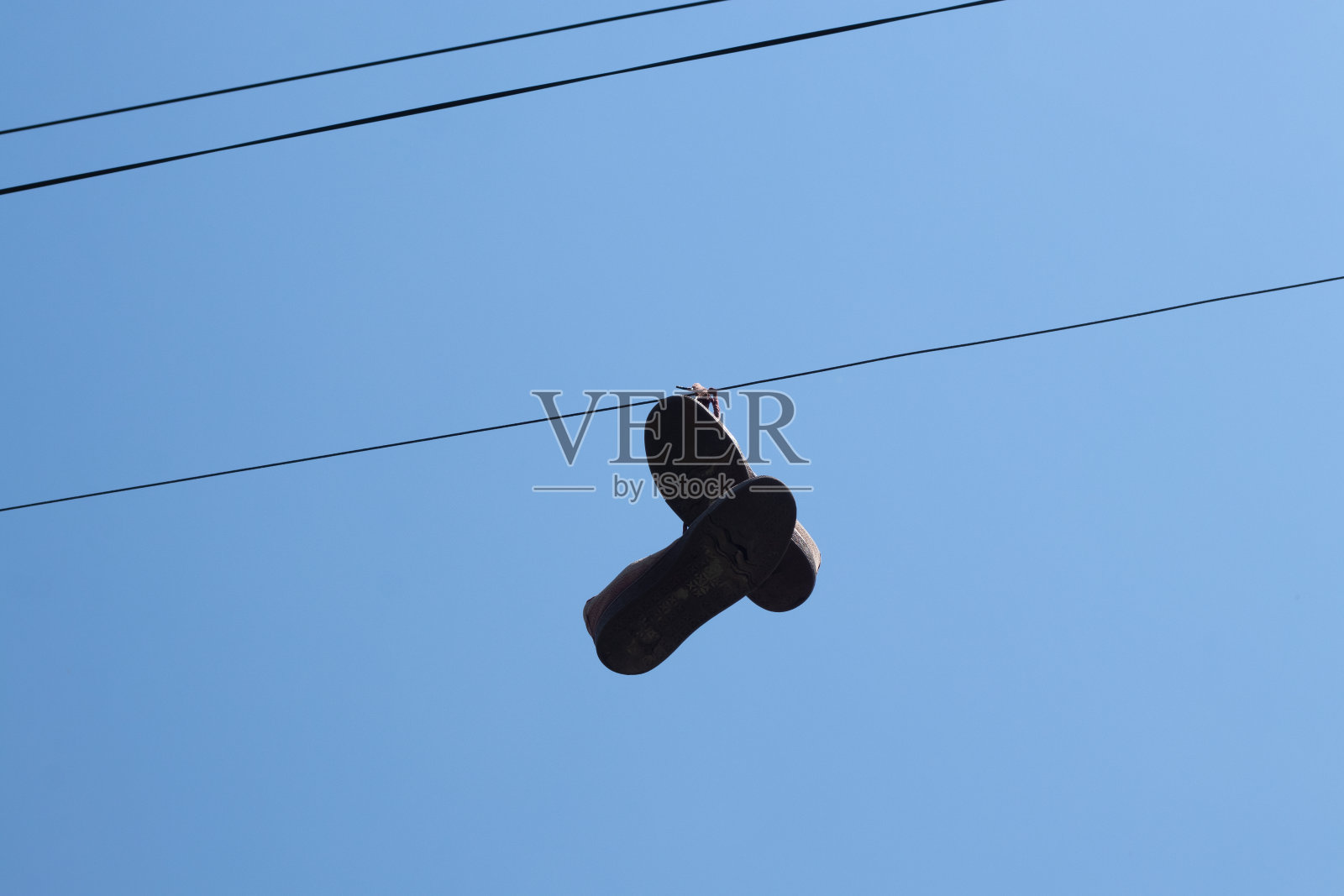 蓝色的天空下,又旧又脏的运动鞋挂在杆子上的电线上照片摄影图片