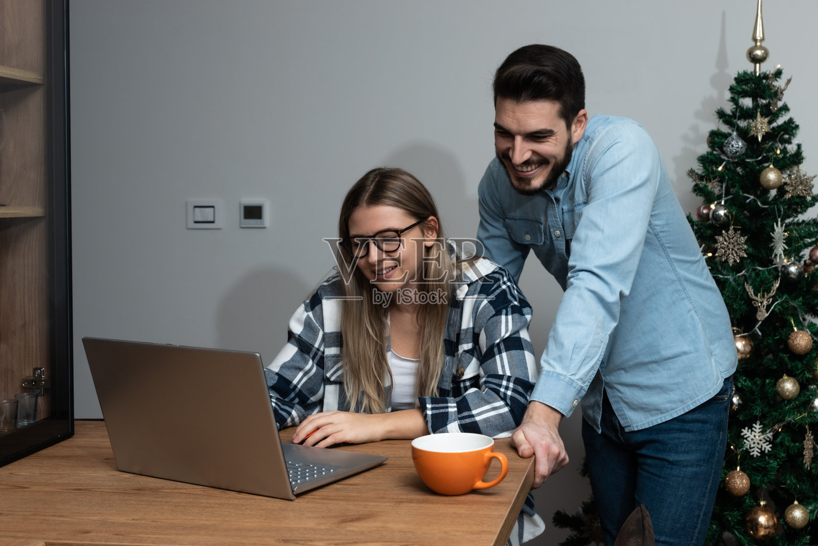 年轻夫妇自由职业者在新年或平安夜在公寓的笔记本电脑上装饰的树在网上工作。独居男女与家人朋友视频通话照片摄影图片