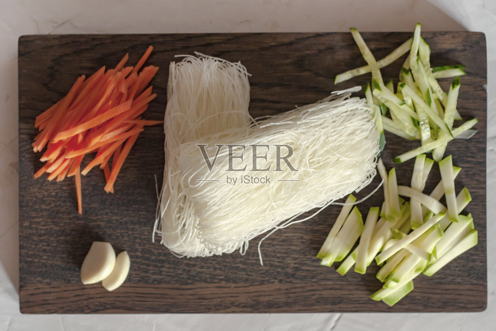 生的韩国淀粉面条和切碎的蔬菜(胡萝卜,黄瓜,西葫芦)放在木板上,灰色背景上的特写,平铺。照片摄影图片