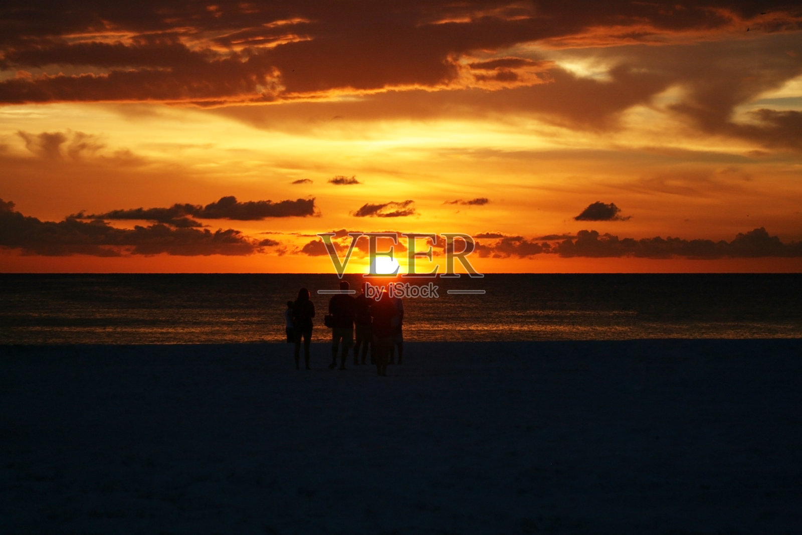 一小群人在海滩上看日落剪影与戏剧性的天空照片摄影图片