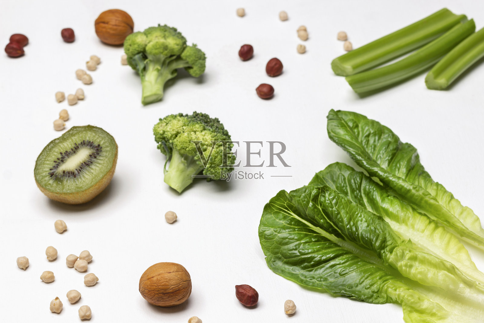 生菜叶,芹菜杆,半个猕猴桃和白色背景的坚果。照片摄影图片