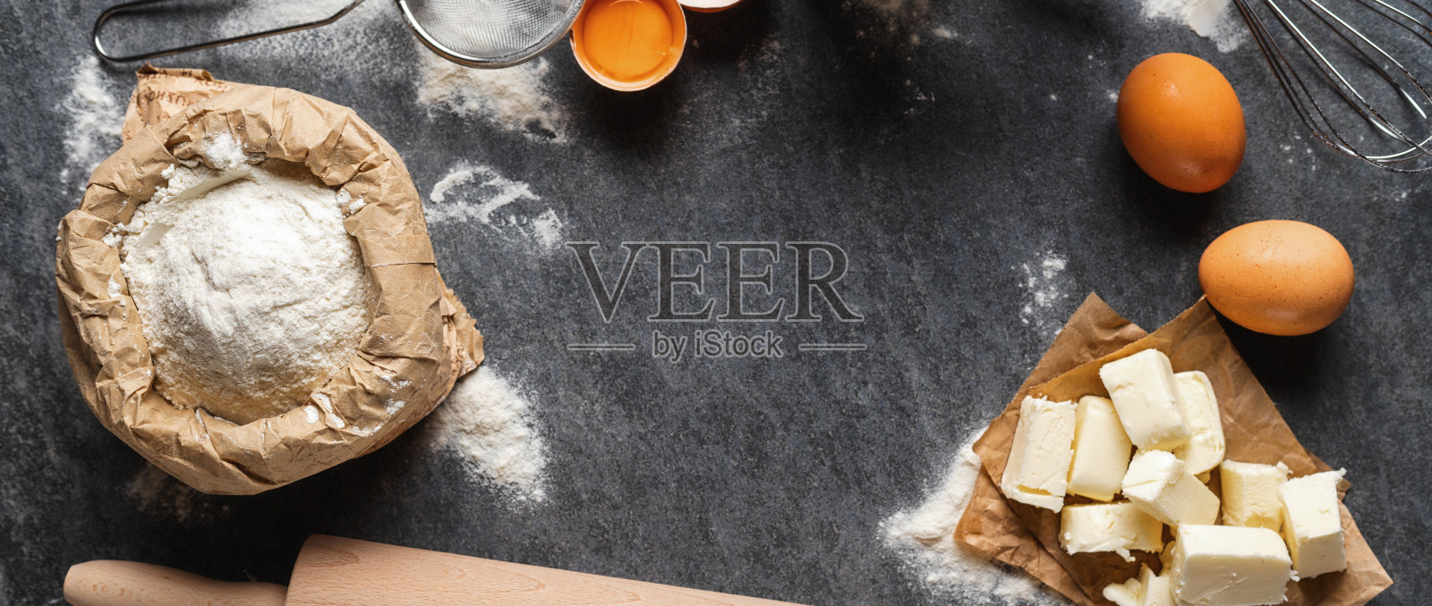 烘烤面团的原料,纸袋面粉,黄油和鸡蛋,擀面杖和筛子在黑暗背景俯视图照片摄影图片