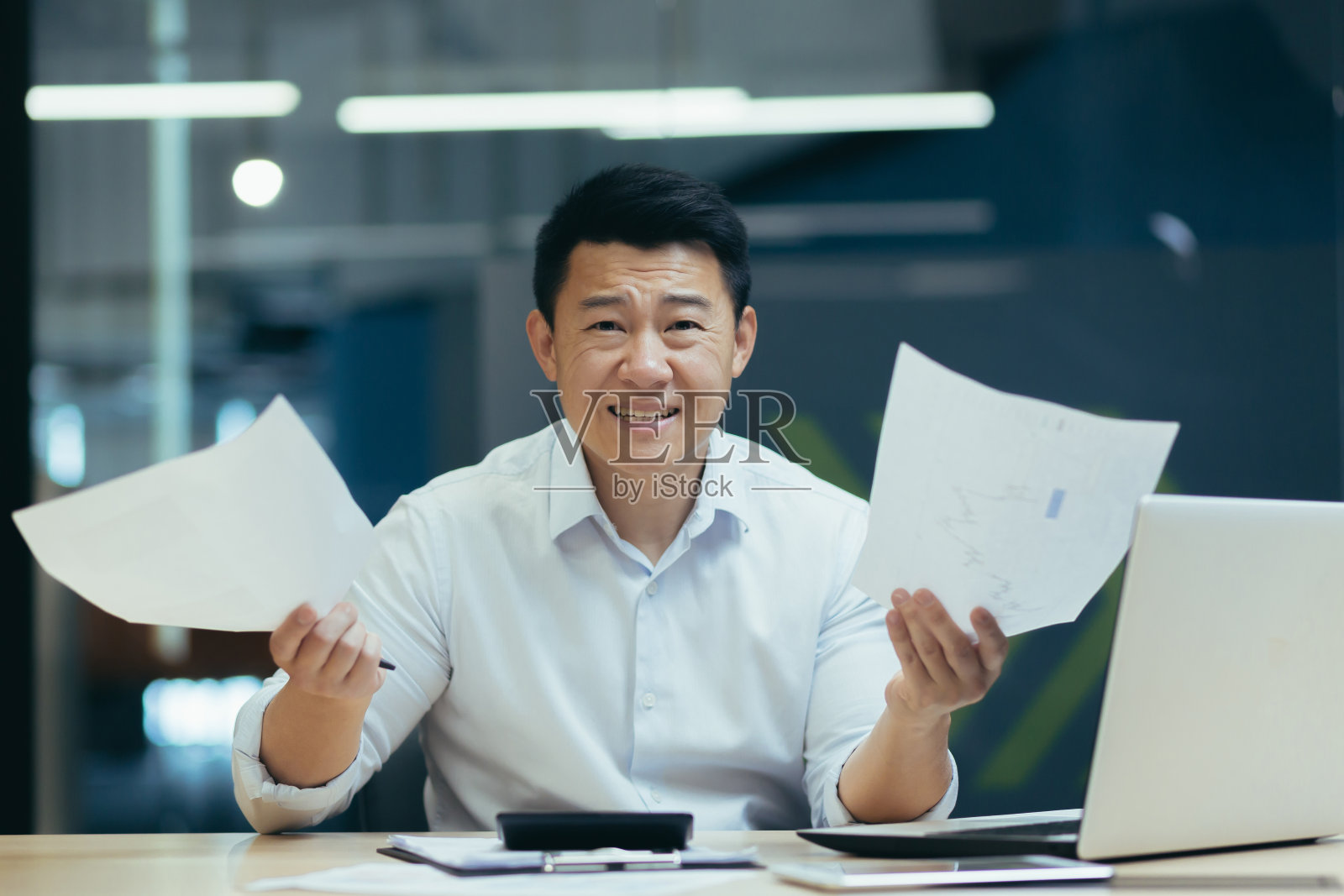 一个忧心忡忡的亚洲商人,正坐在办公室里,手里拿着文件,财务出了问题照片摄影图片
