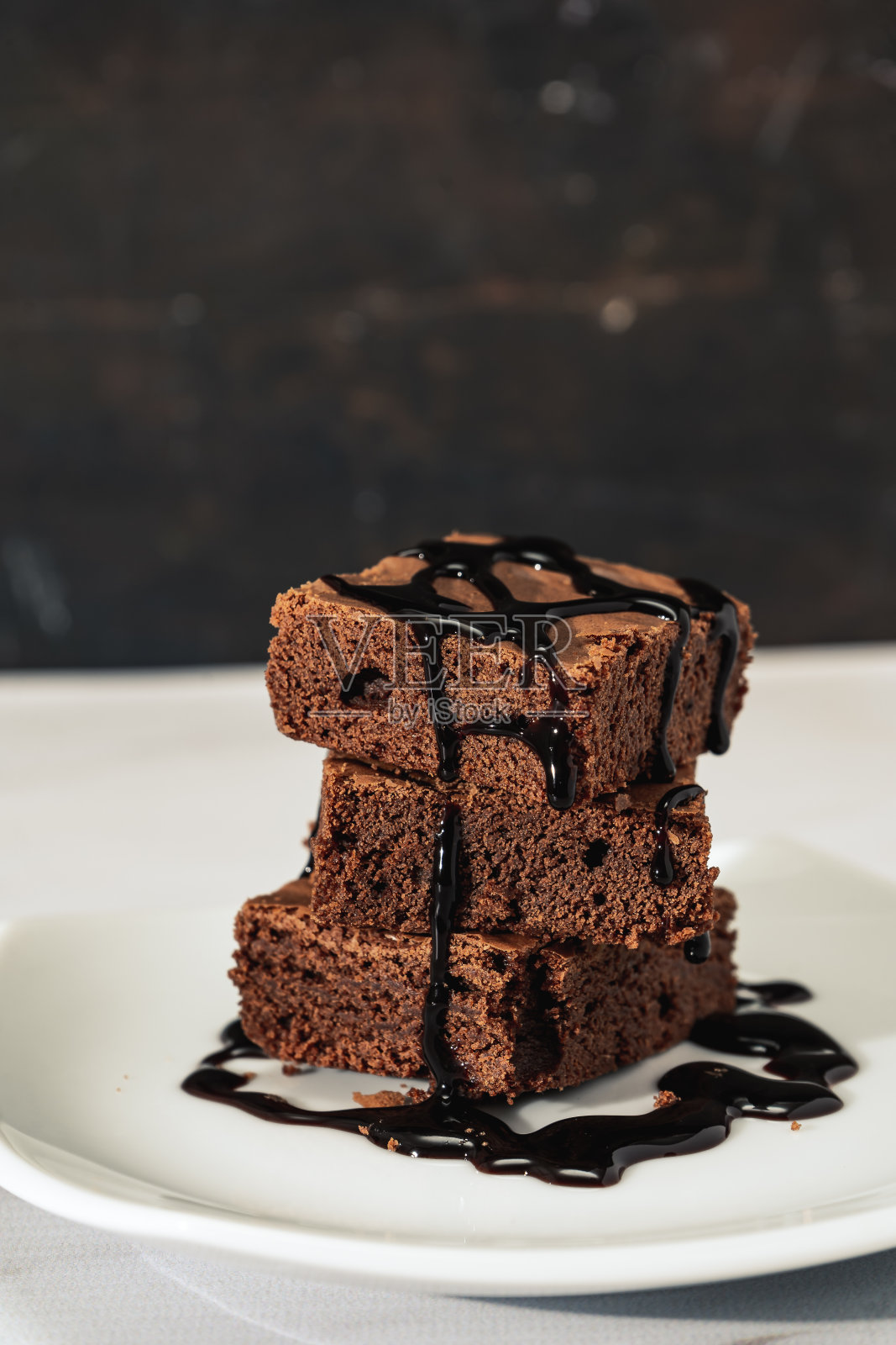 一堆巧克力布朗尼和巧克力酱,放在大理石桌子上的白色盘子上。垂直方向。副本的空间。较低的观点。照片摄影图片