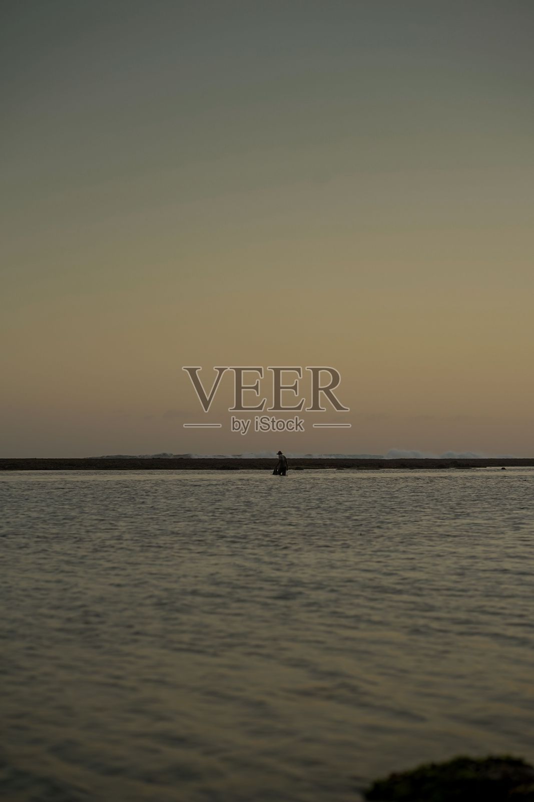 垂直拍摄一个人在远处一个宁静的海上垂钓黄昏照片摄影图片