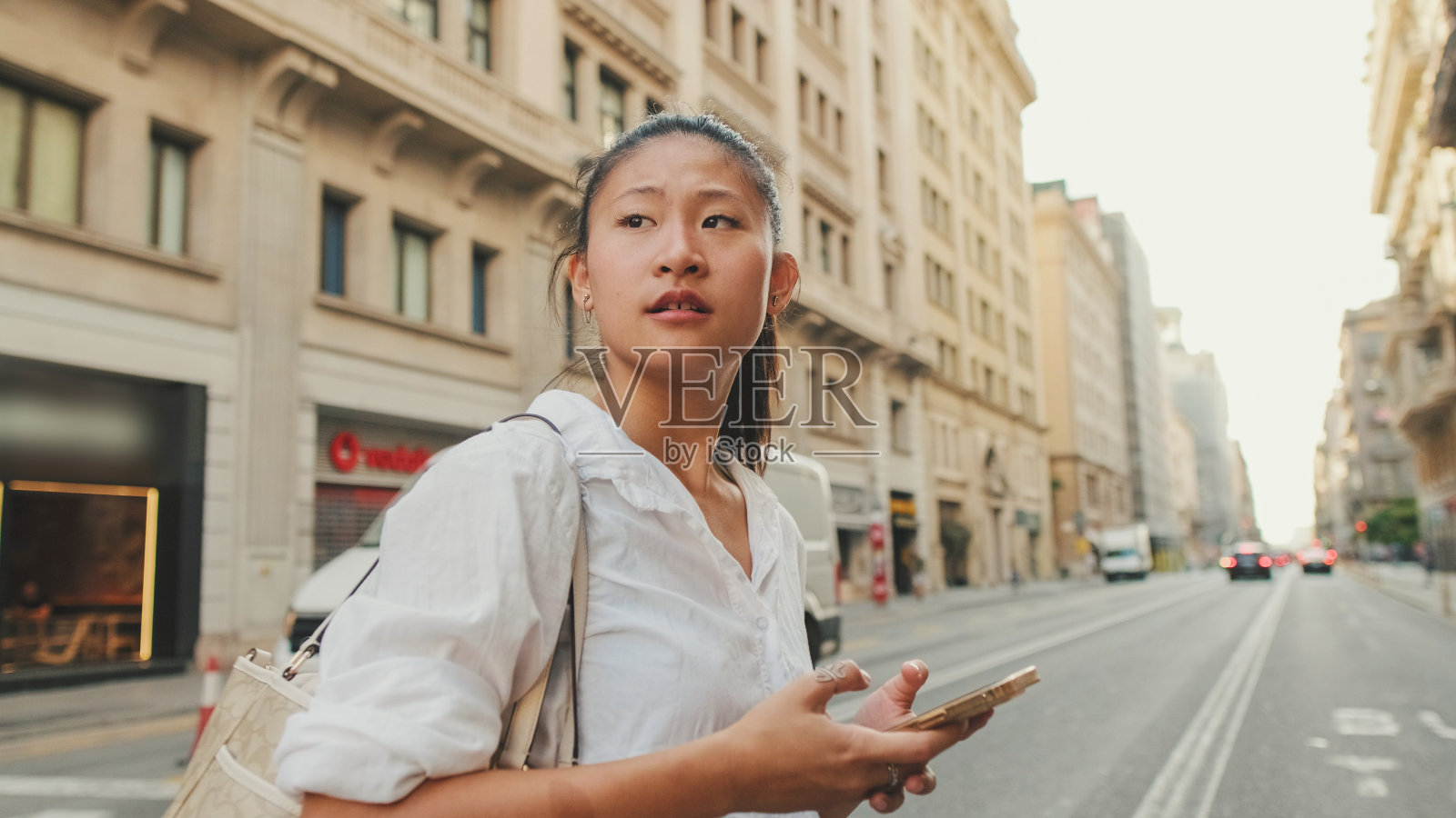 一名年轻女子在人行横道处过马路,手里拿着手机照片摄影图片