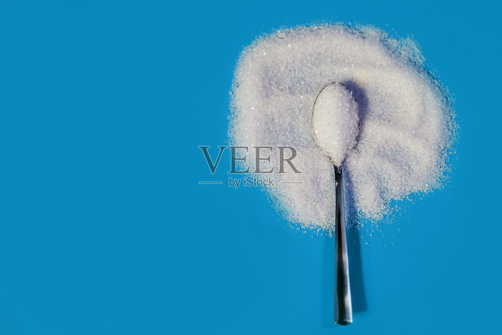 糖粉在蓝色的背景上,用一个金属勺子,勺子放在糖上照片摄影图片