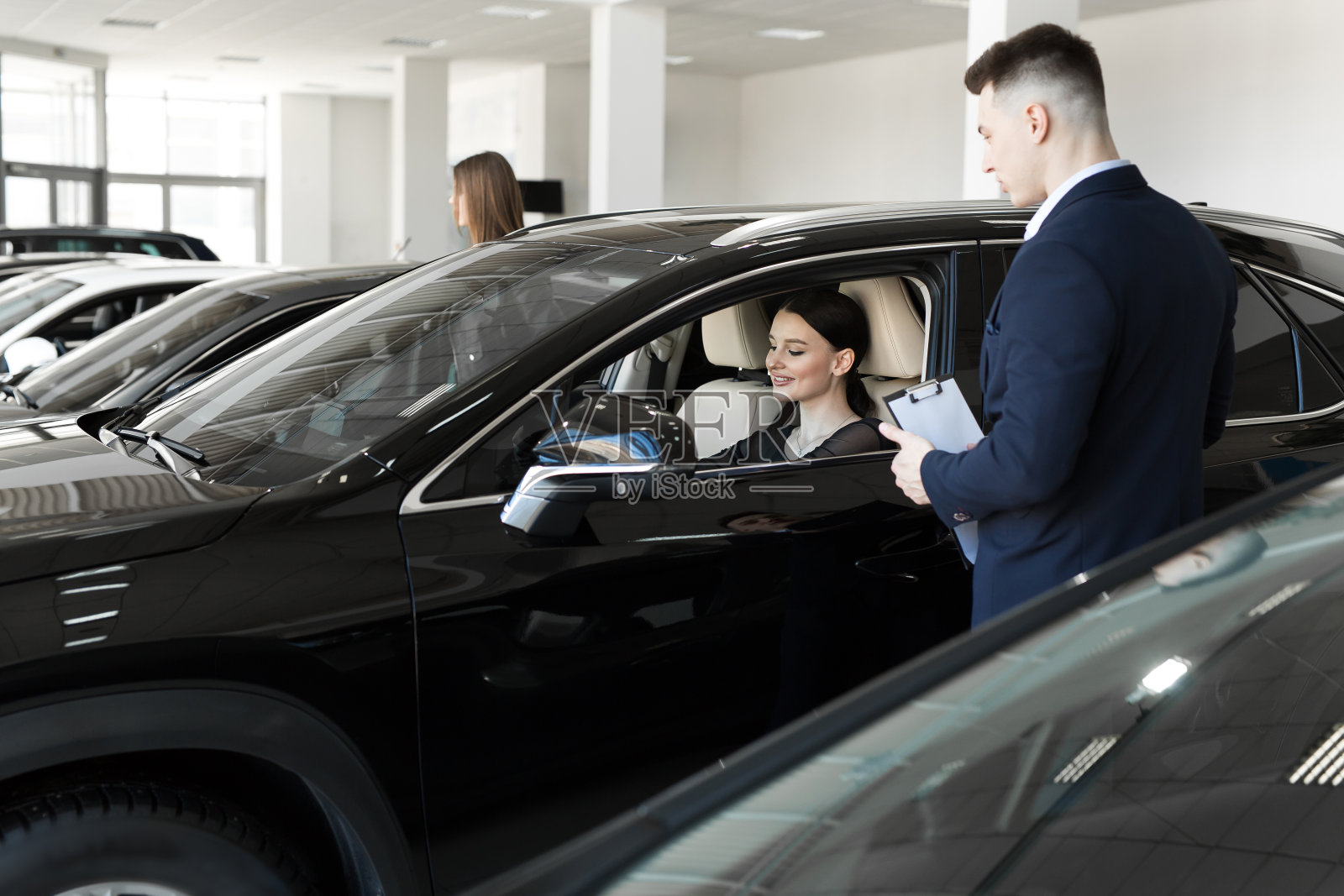 年轻美丽的女人坐在车里,手握方向盘的侧面。她微笑着与汽车经销商经理交谈。代表汽车内部的汽车代理商照片摄影图片