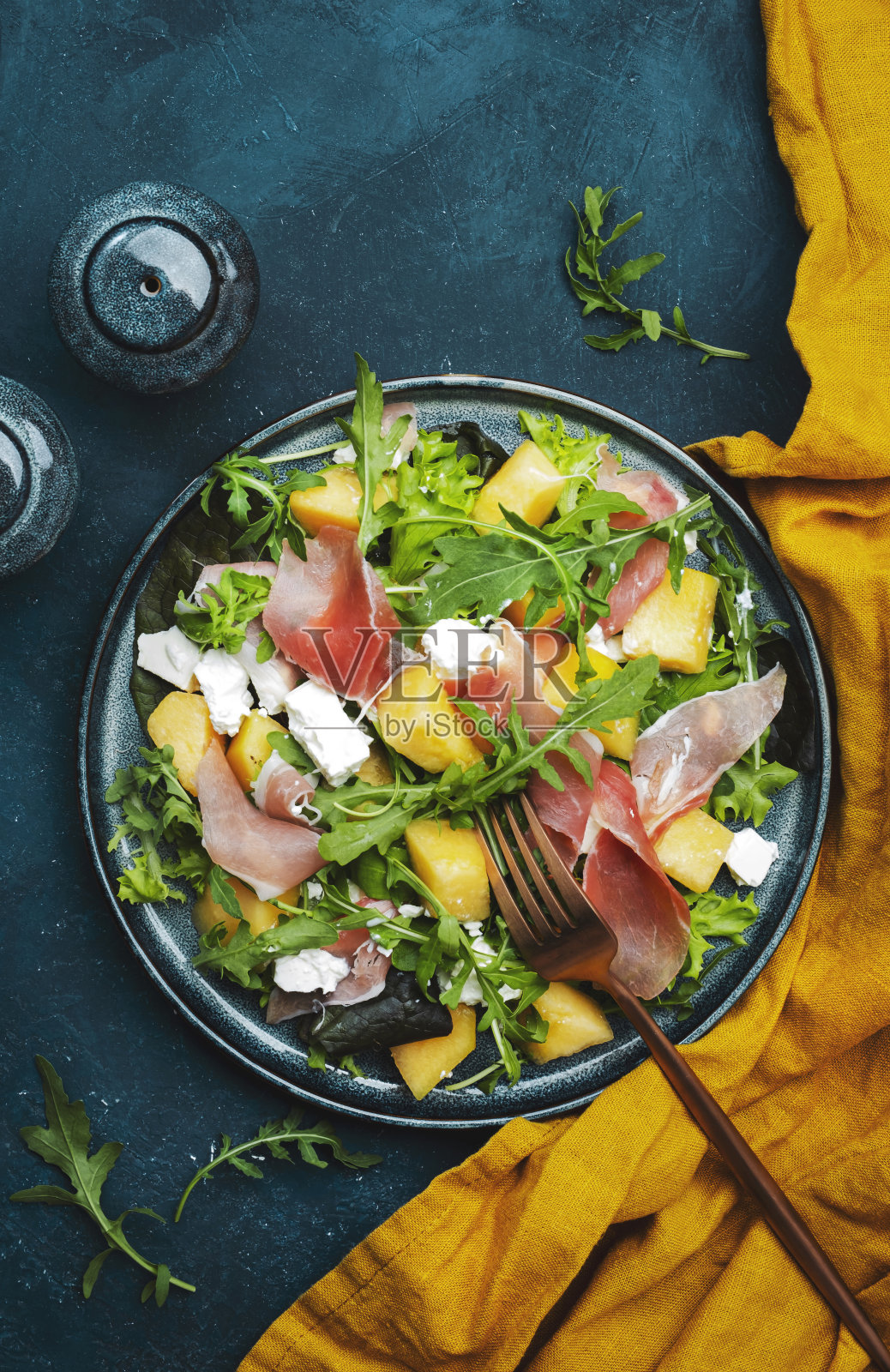 美味的夏季新鲜沙拉与哈密瓜,熏火腿,软奶酪和芝麻菜在蓝色的桌子背景,俯视图,复制空间照片摄影图片