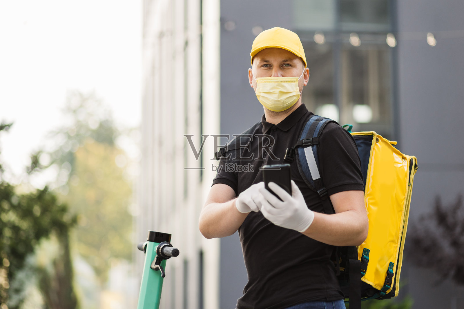 戴着口罩骑滑板车的送货员在城市中使用智能手机的正面照照片摄影图片
