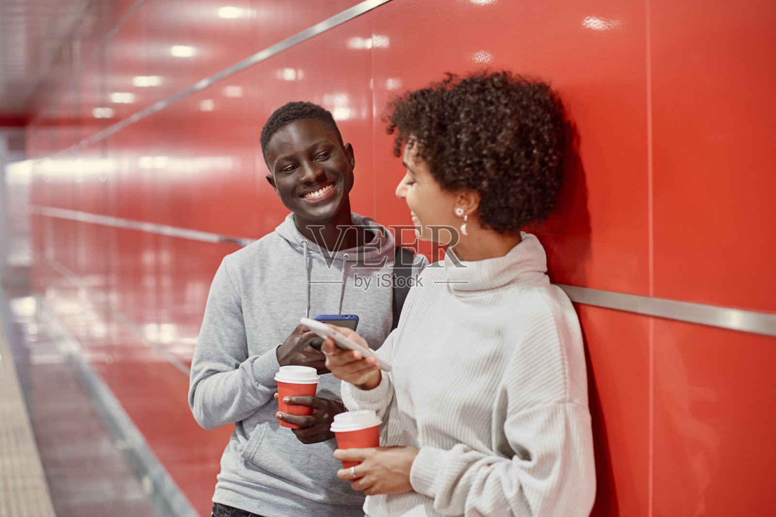 拿着智能手机、喝着外卖咖啡等地铁的年轻人。照片摄影图片