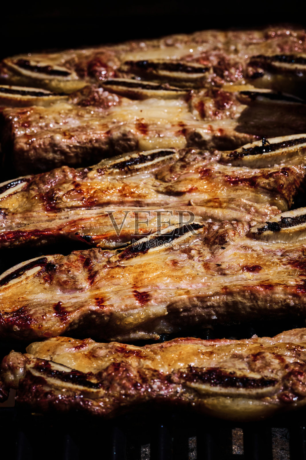 多汁的牛肉排骨和猪排骨在燃气烧烤架上的火上慢慢地烤着照片摄影图片