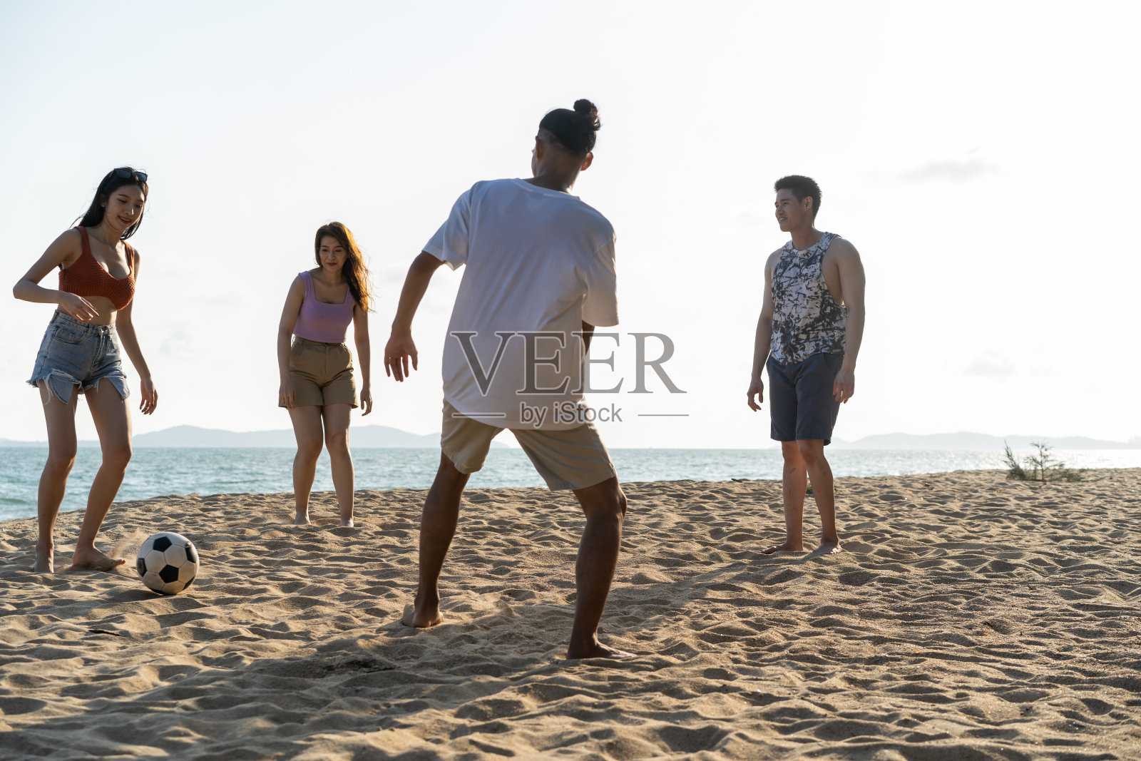 一群亚洲青年男女在沙滩上一起踢足球。有吸引力的朋友旅行者感到快乐和放松,有一个足球比赛,而旅行度假在热带海岛。照片摄影图片