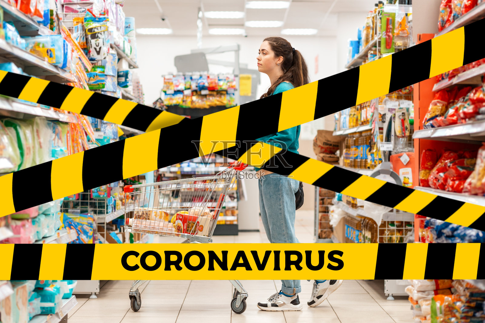 不要交叉。屏障胶带-隔离,隔离。一名穿着休闲服装的年轻白人女子推着一辆购物车,在一排排的食品货架之间穿行。购物的概念和冠状病毒照片摄影图片