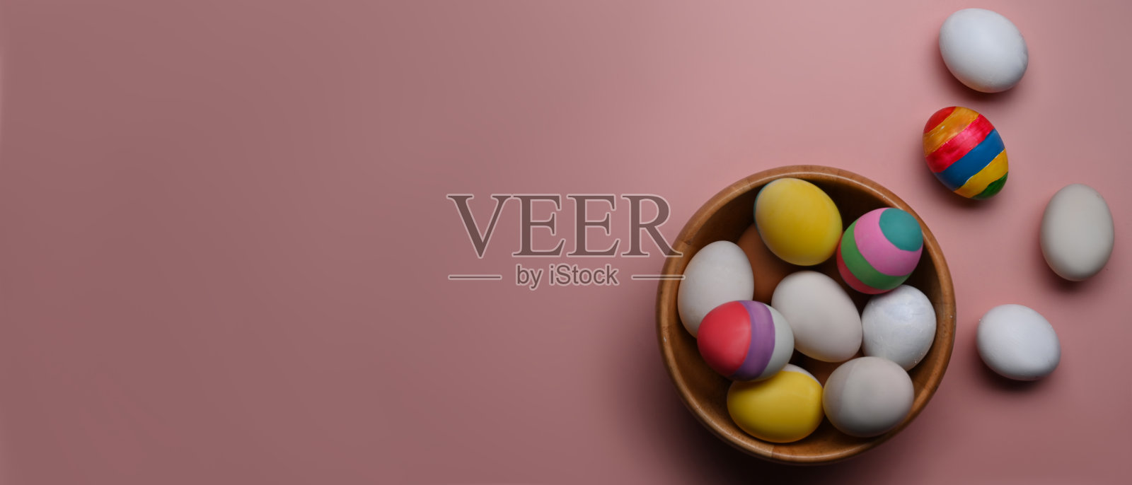 一个装满复活节彩蛋的木碗在粉红色的背景与文本或设计的复制空间。照片摄影图片