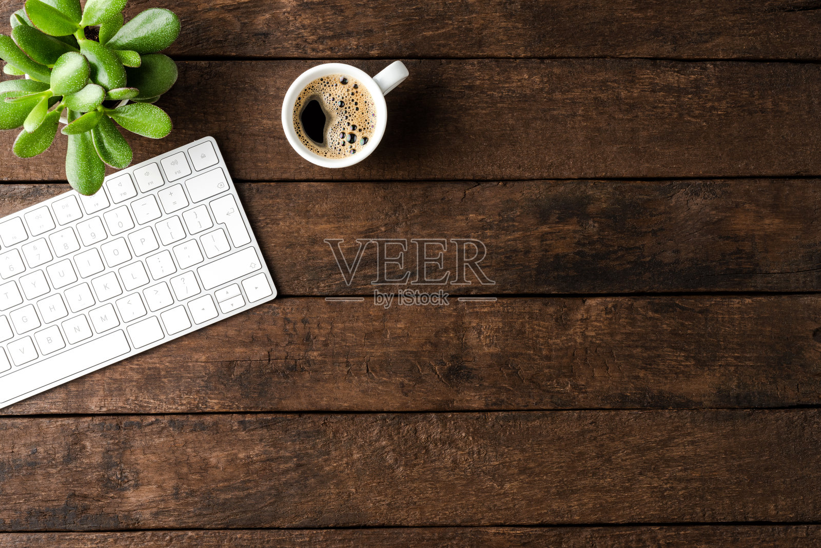 电脑键盘和咖啡杯放在木桌上。办公室桌面照片摄影图片