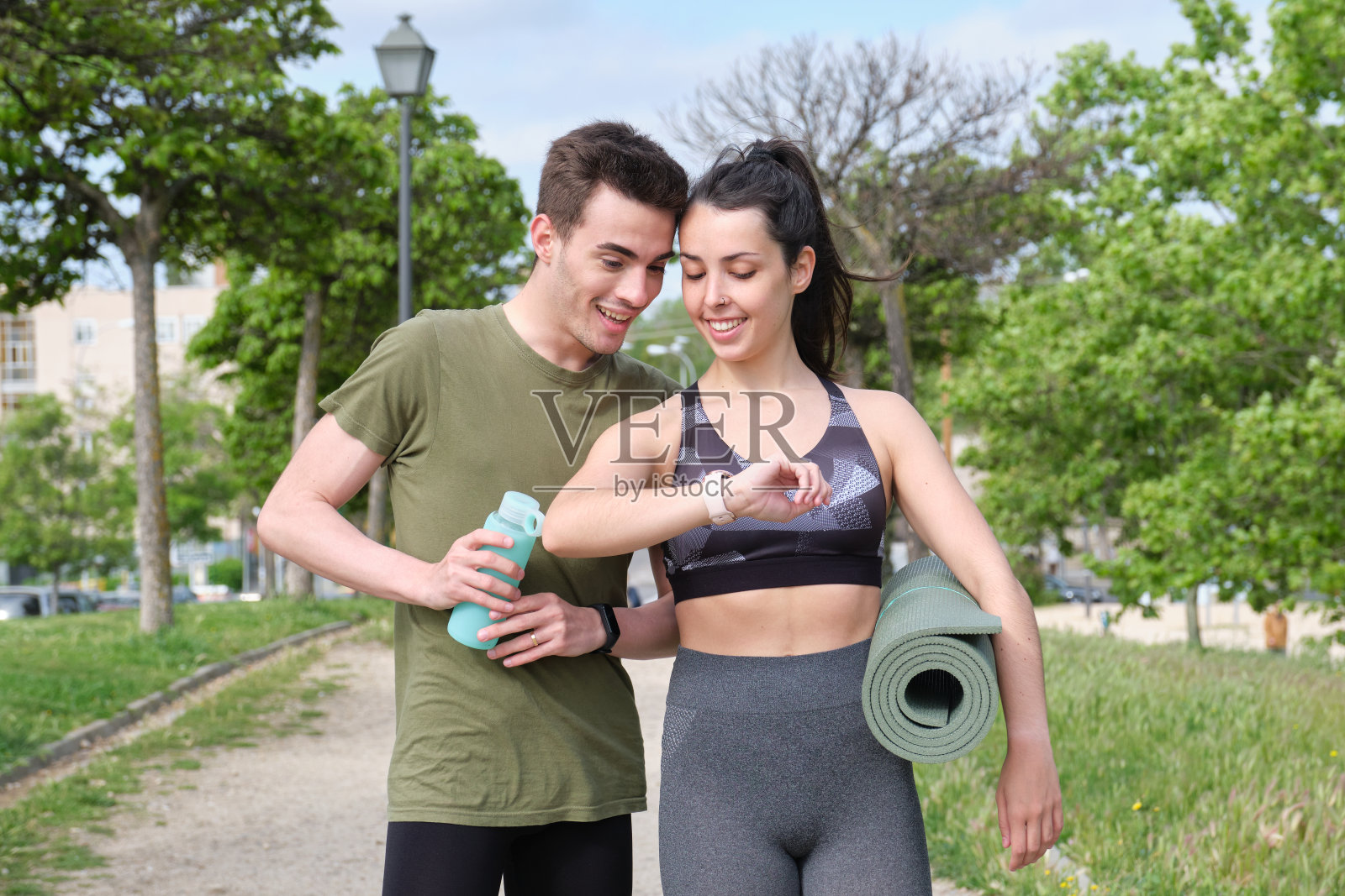 快乐的年轻运动夫妇看着智能手表,而站在公园。照片摄影图片