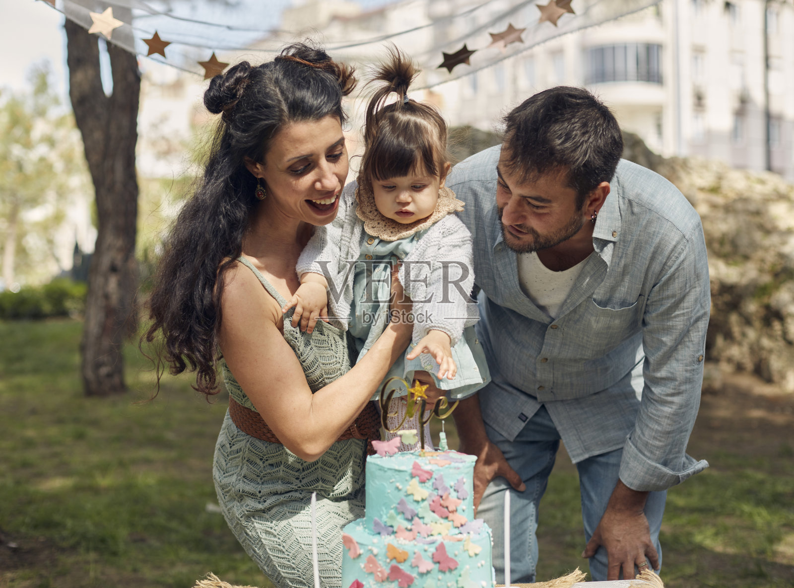 在花园里为小女儿庆祝生日,爸爸妈妈一起吹生日蛋糕。照片摄影图片