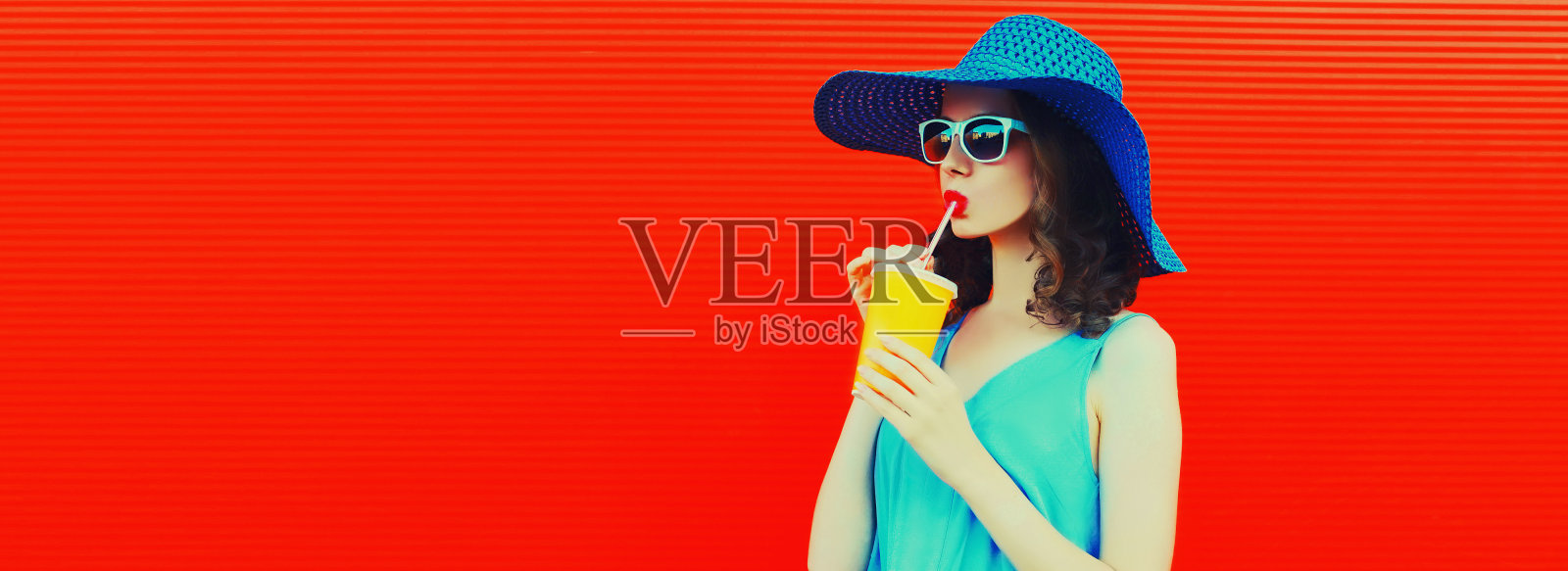 美丽的年轻女子的肖像喝新鲜果汁从杯子戴着夏天的帽子在红色的背景,空白的拷贝空间的广告文字照片摄影图片