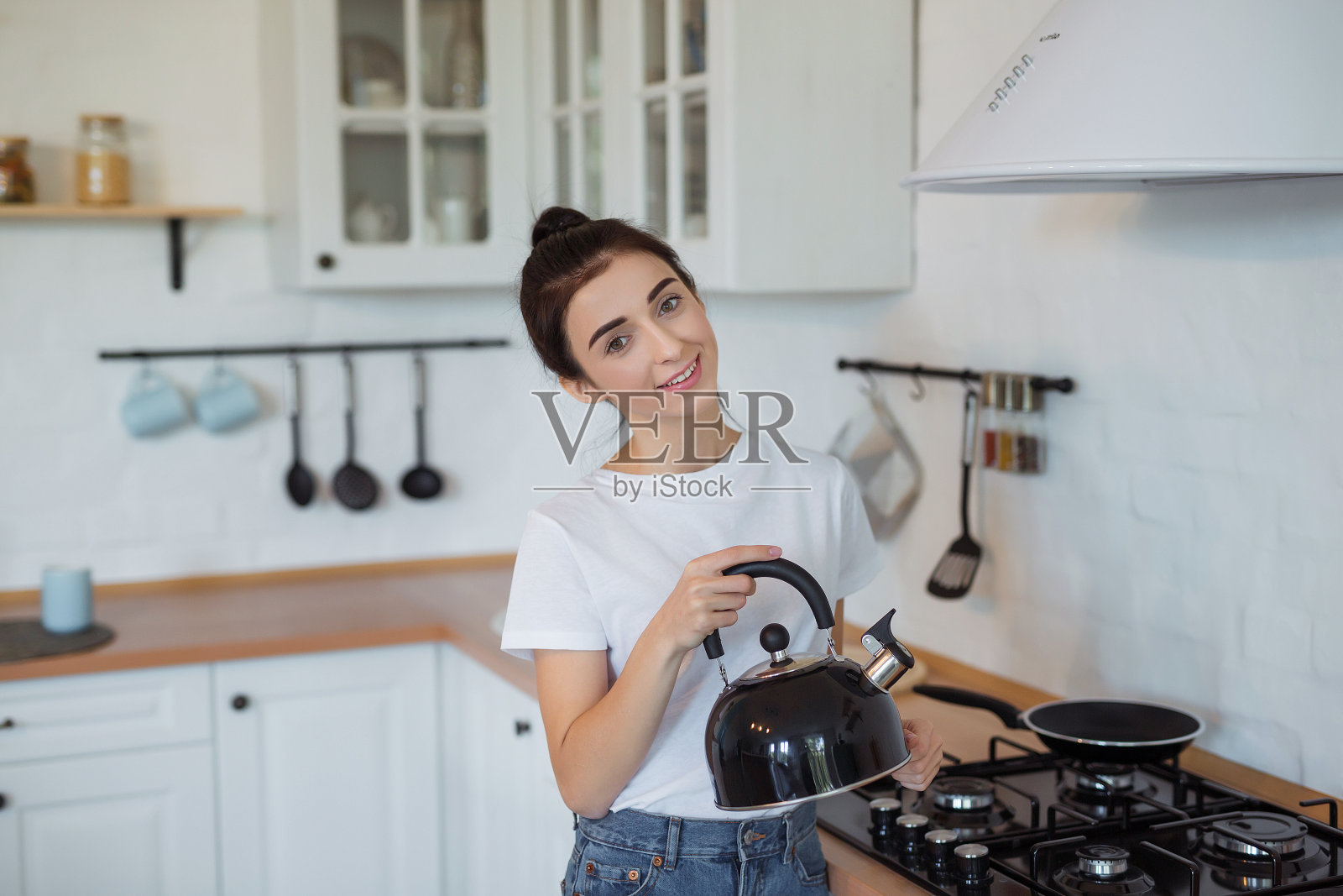 在现代阁楼厨房里,女人触摸炉子上的茶壶。拿着水壶的美女照片摄影图片