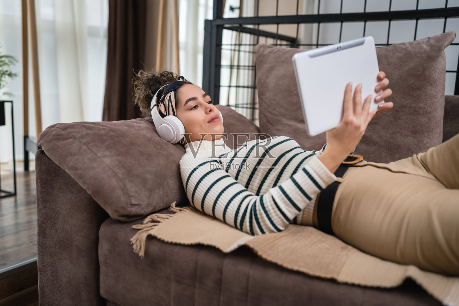 一名年轻女子戴着耳机躺在床上,手里拿着平板电脑照片摄影图片