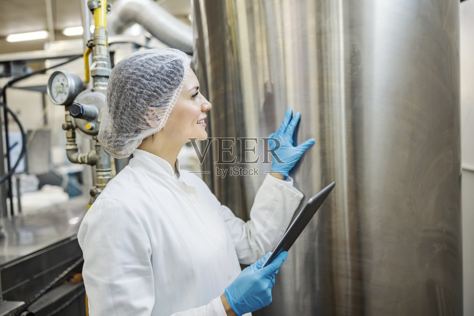 一位牛奶加工厂的专家手里拿着药片,正在监视牛奶箱。照片摄影图片