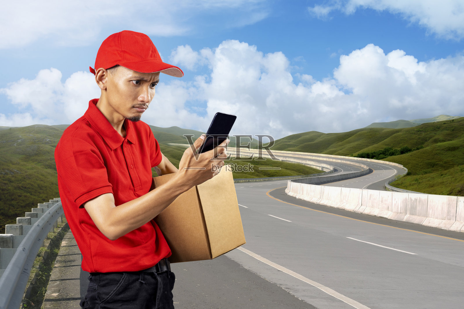 一个戴着帽子、拿着手机的快递员拿着一个包裹照片摄影图片