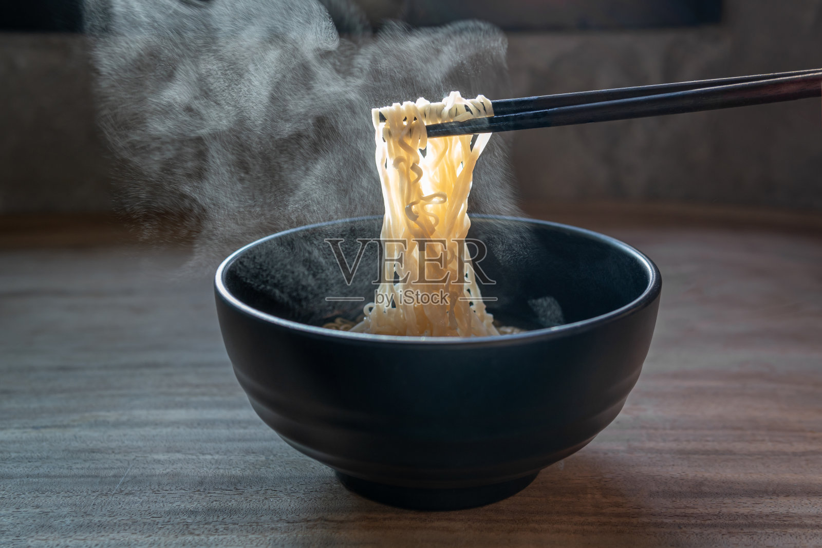 用木筷子夹起黑色背景上有蒸汽和烟雾的面条。韩国,日本,中国,越南和亚洲面条食品概念照片摄影图片