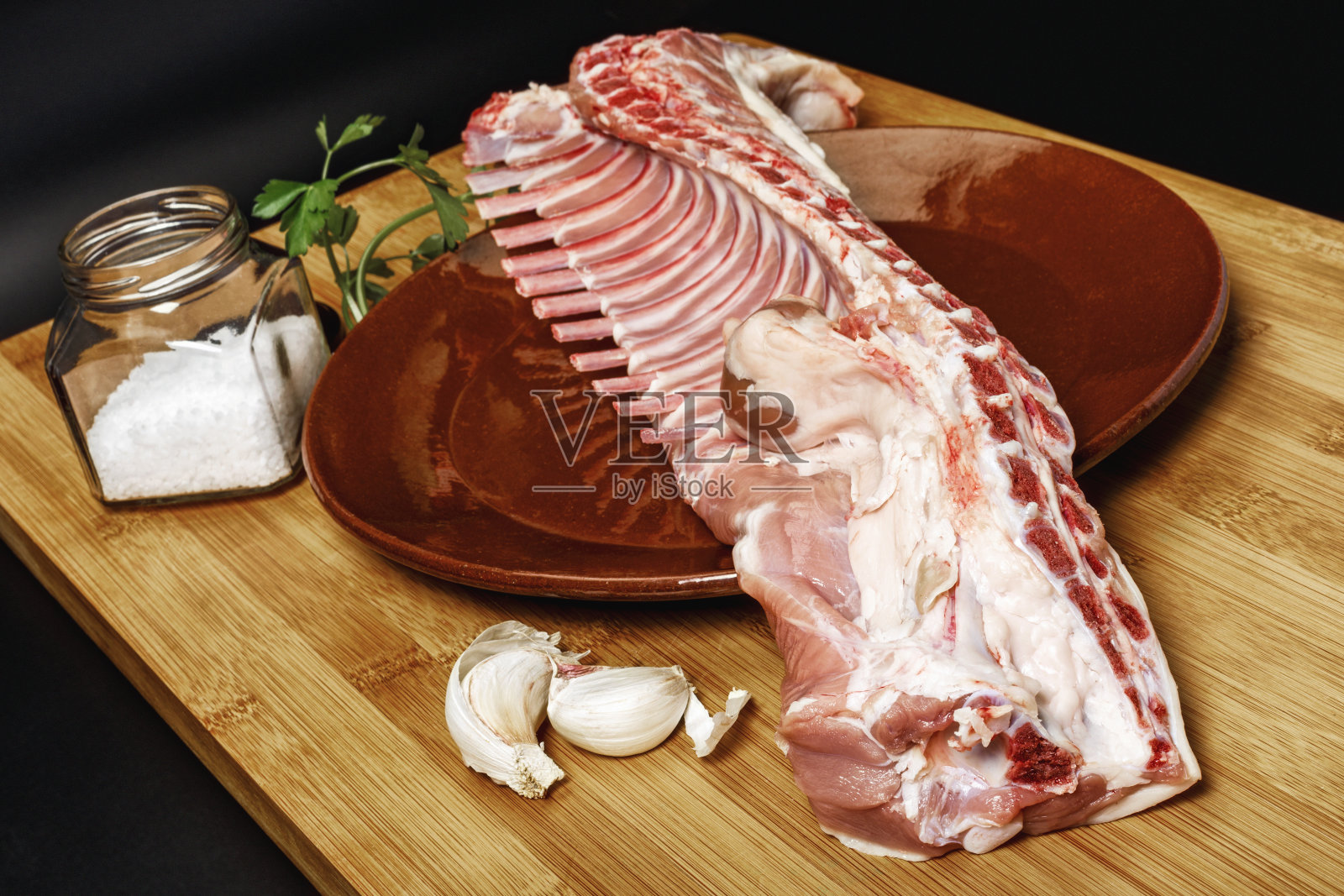 近距离拍摄的生羊肉放在盘子上,与盐,大蒜和欧芹一起放在砧板上照片摄影图片