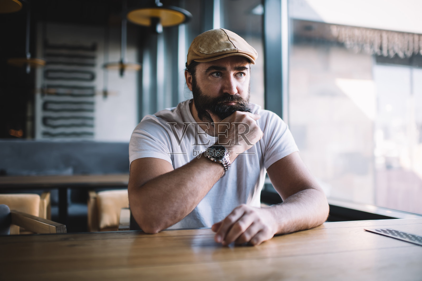 严肃的白人成熟男子咖啡馆的客人坐在窗前思考着想法和未来的计划,严肃的胡子小企业主戴着帽子,戴着时髦的手表照片摄影图片
