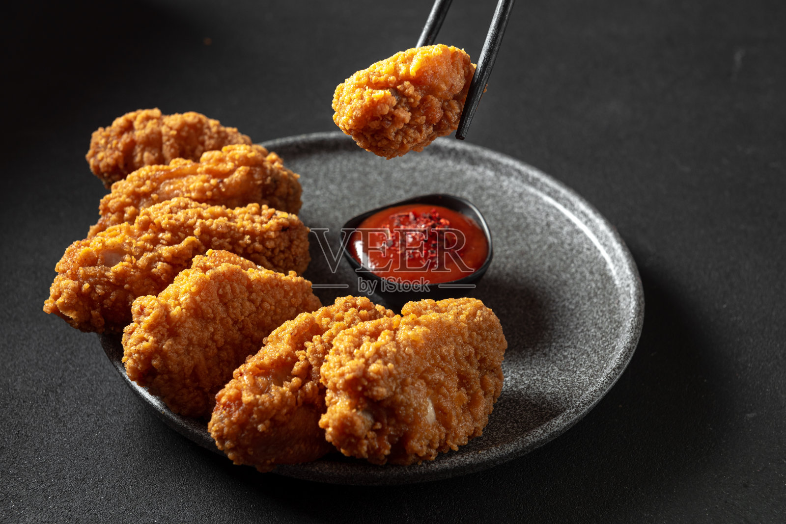 深色背景的亚洲鸡面糊。中国的筷子夹住一块鸡肉照片摄影图片