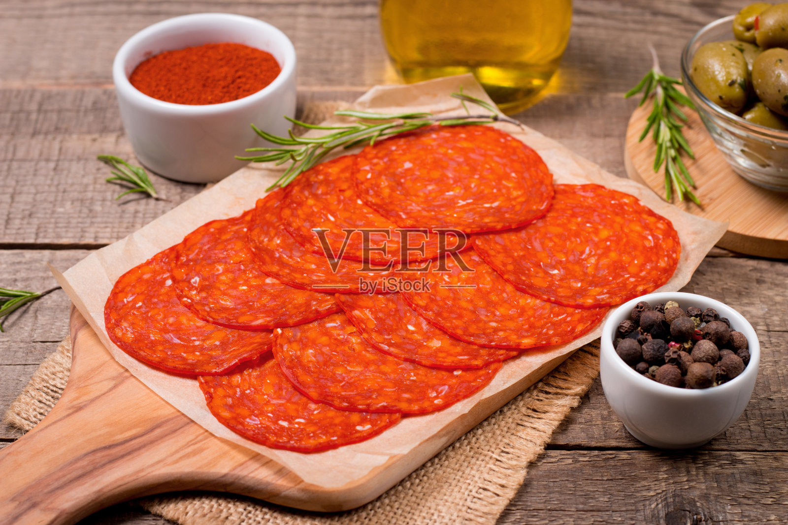 切薄的西班牙香肠和意大利腊肠。木质背景的西班牙腊肠配上香料、辣椒粉、迷迭香和橄榄。辣的食物。开胃菜和开胃肉。照片摄影图片