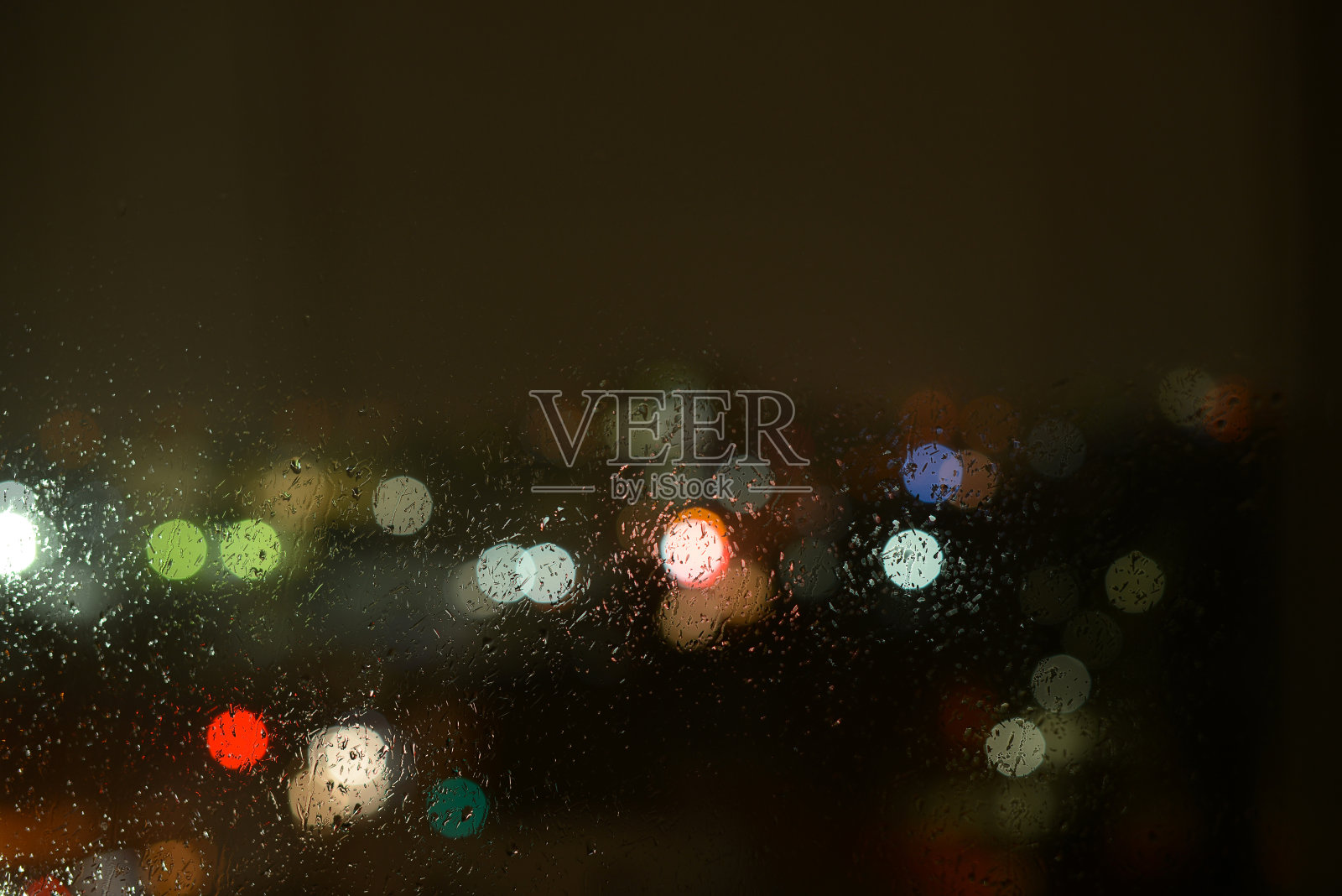 窗户玻璃上的雨滴和夜晚或夜晚城市的不集中的灯光。雨中玻璃背后的夜城背景照片摄影图片