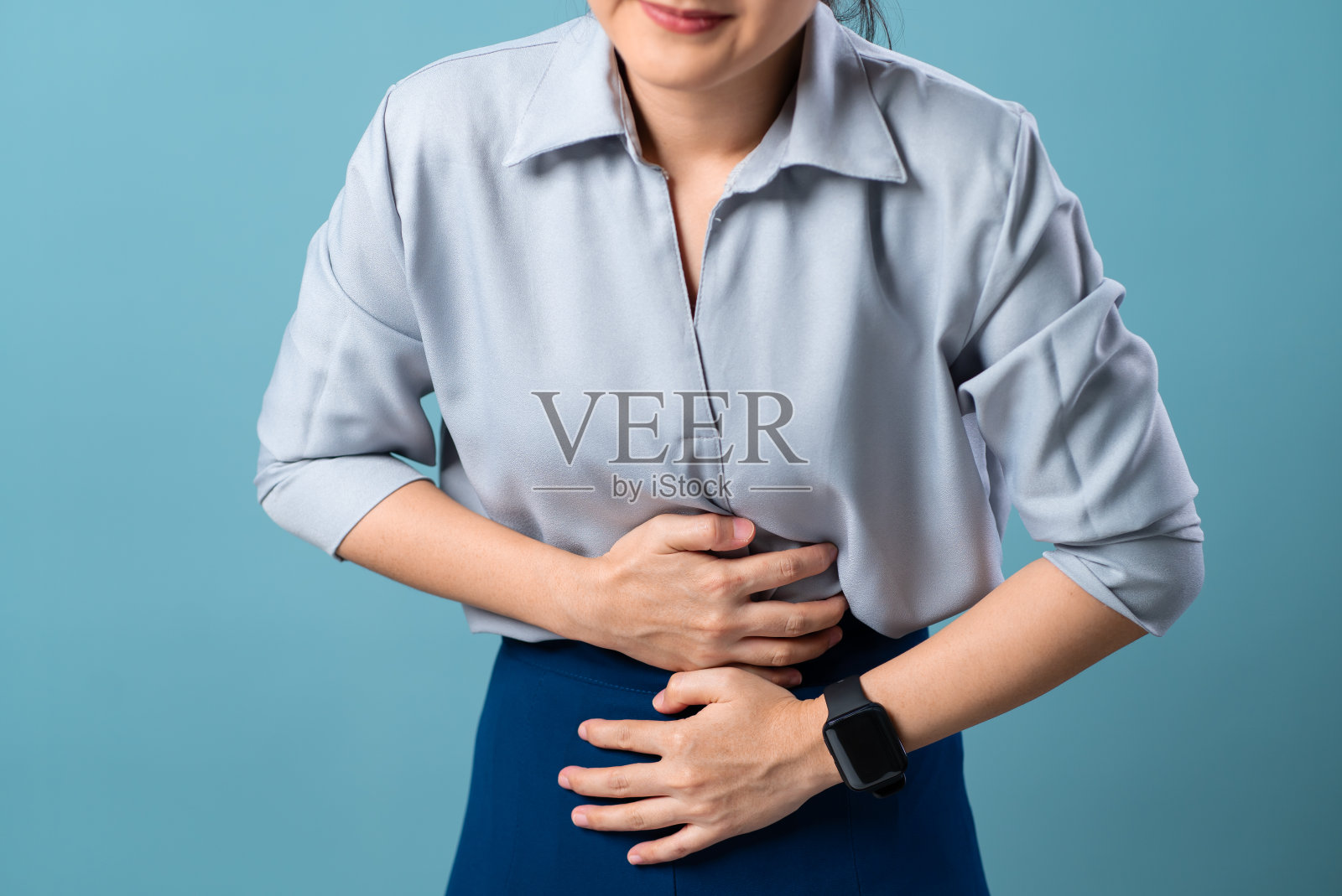 特写镜头,一个女人胃疼,孤立地站在蓝色背景上。照片摄影图片