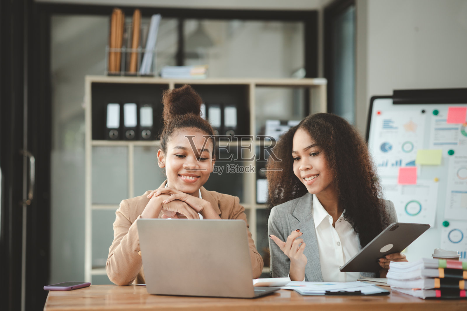 两个美国女人在一家初创公司的办公室里一起工作。他们正在一个联合部门举行头脑风暴和计划会议,由女性主导。妇女的工作观念。照片摄影图片