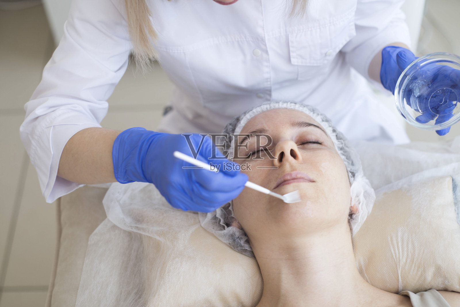 在水疗沙龙里,美容师用刷子把面霜涂在病人脸上照片摄影图片