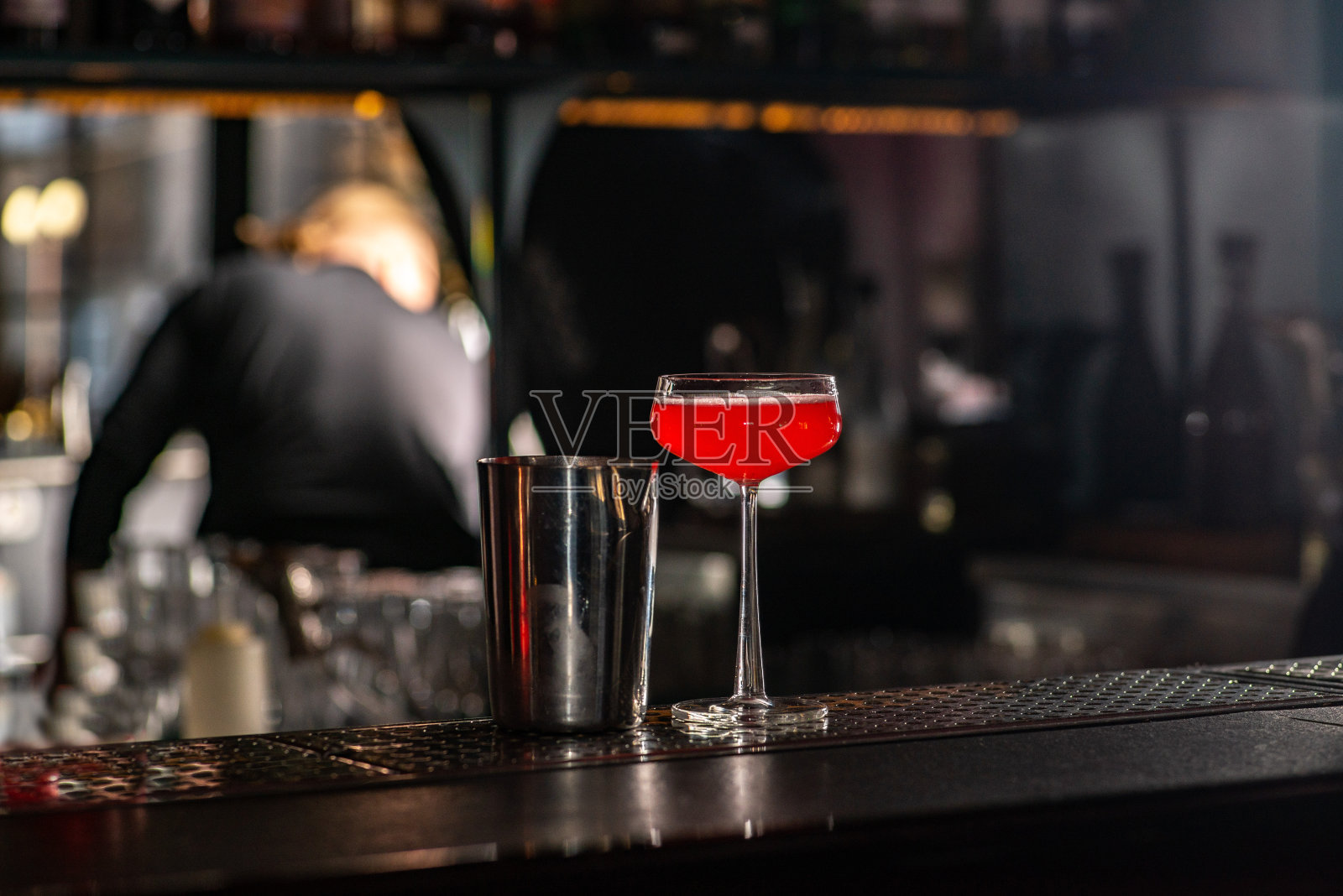 吧台上有红色鸡尾酒和调酒器。酒吧夜生活氛围浓厚。照片摄影图片