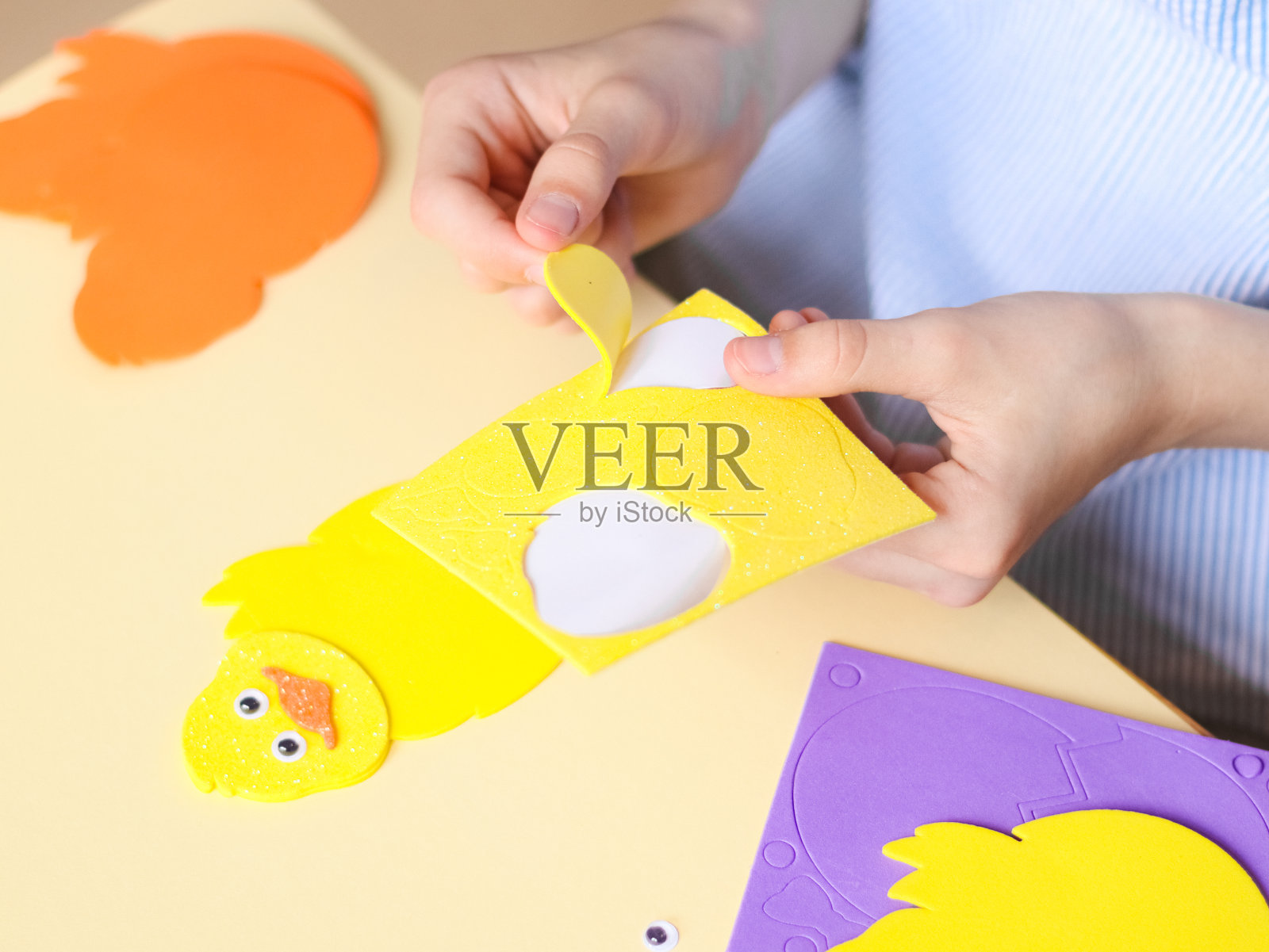 一个白人少女的手正在剥掉黄色鸡毛毡上的翅膀贴纸照片摄影图片