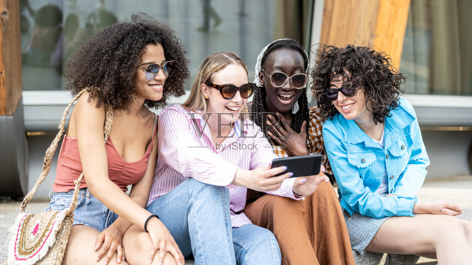城市里的四个Z世代少女,年轻女性坐在城市的长椅上,用智能手机进行社交网络照片摄影图片