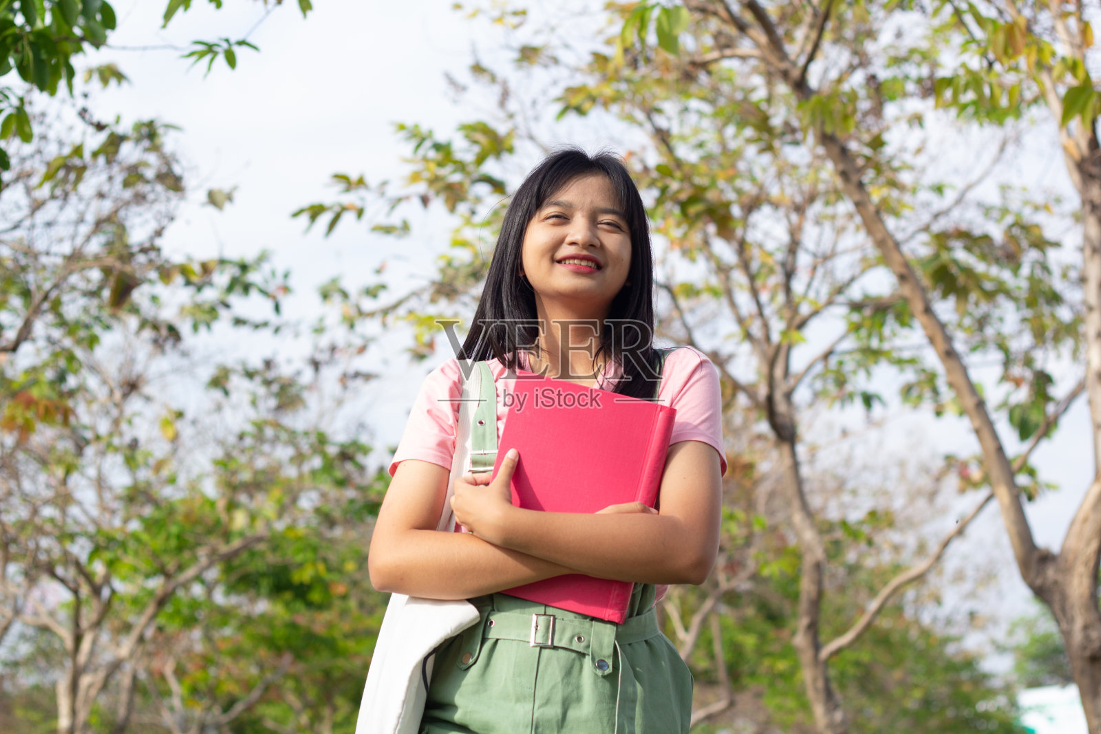 学生女孩拿着书走在绿色公园。照片摄影图片