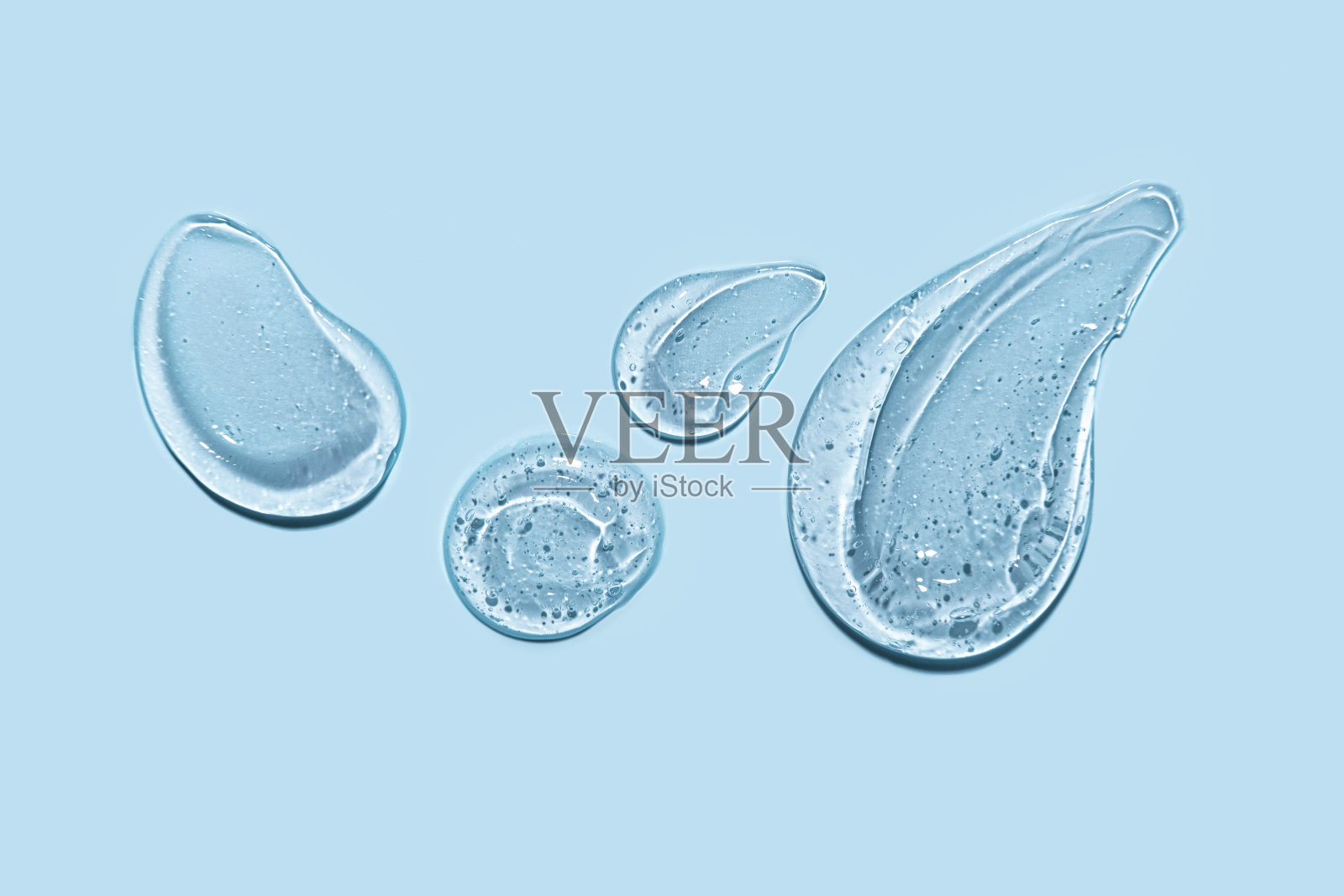 皮肤护理霜,面部精华色块涂抹在蓝色背景。透明凝胶精华产品涂抹涂抹特写。透明滴凝胶在蓝色背景。照片摄影图片