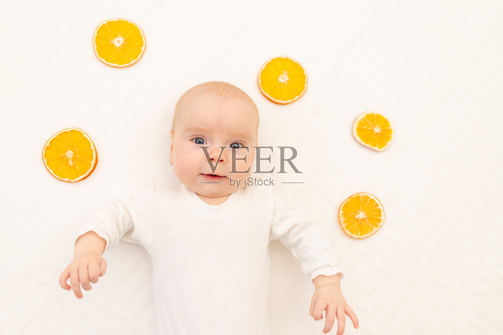 一个婴儿的肖像在白色背景与橙色。儿童床上用品。8个月。一个穿着紧身睡衣的健康孩子儿童柑橘过敏照片摄影图片